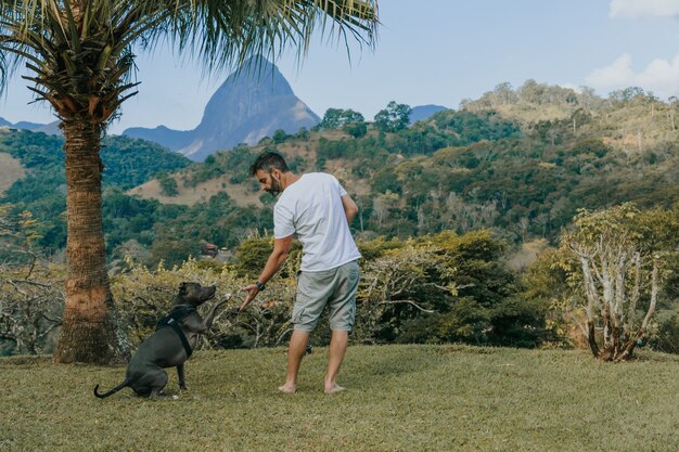 Een man en een Pit Bull-hond spelen en bewonderen de natuur en de bergen van PetrÃ,polis, in Rio de Janeiro, Brazilië. Liefdevolle relatie tussen mens en dier.