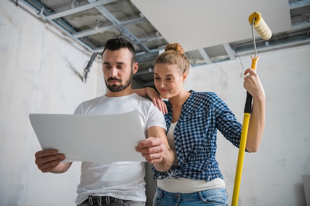 Een man en een vrouw glimlachen en kijken naar het werkplan tijdens de renovatie van een appartement