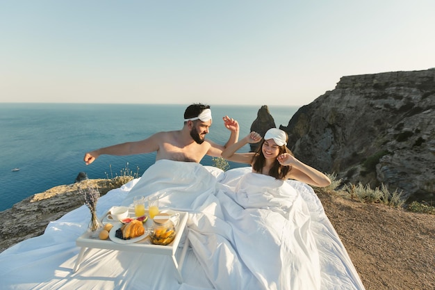 Een man en een vrouw hebben plezier in een wit bed op een klif met uitzicht op de zee en jachten