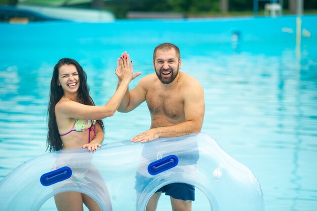 Een man en een vrouw in een rubberen opblaasbare cirkel staan tegen de achtergrond van het zomerbad van het waterpark en klappen in hun handen.