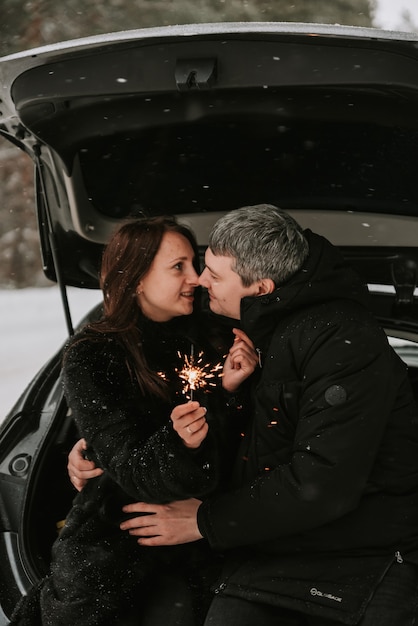 Een man en een vrouw op de achtergrond van een besneeuwd bos in een sneeuwval in de kofferbak van een auto