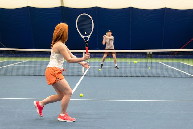 Een man en een vrouw tennissen op een binnenbaan. De coach maakt een pitch, achteraanzicht