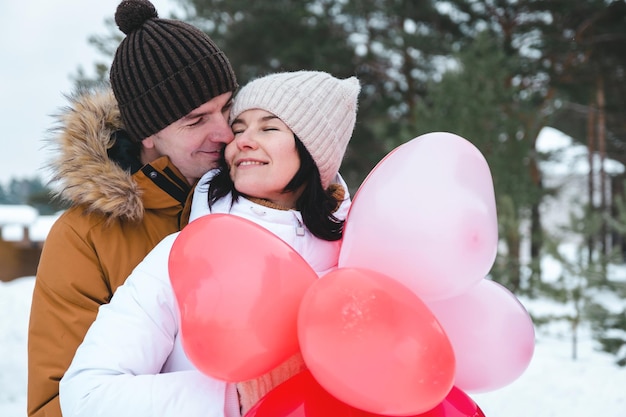 Een man en een vrouw verliefd op een buitenafspraakje in de winter in de sneeuw met een geschenk van roze en rode ballonnen in de vorm van een hart. Valentijnsdag, liefde, gelukkig verliefd stel tijdens een wandeling