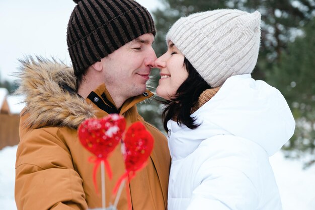 Een man en een vrouw verliefd op een outdoor date in de winter in de sneeuw met een rood decor in de vorm van een hart. Valentijnsdag, liefde, gelukkig verliefd stel tijdens een wandeling, knuffels en kusjes