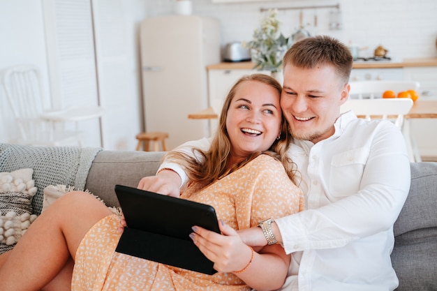 Foto een man en een vrouw zitten thuis op een bank en kijken naar een film op een tablet. een bestelling op internet is online. een echtpaar rust op een pandemische quarantaine.