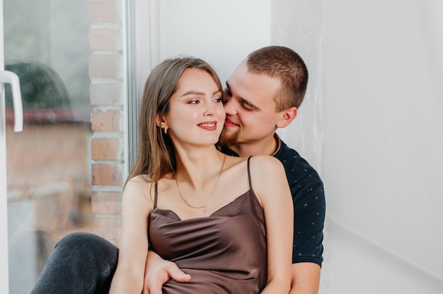 Een man en een zwangere vrouw zitten op een vensterbank en knuffelen elkaar