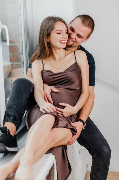 Een man en een zwangere vrouw zitten op een vensterbank en knuffelen elkaar