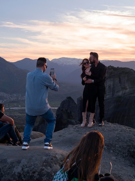 Een man fotografeert een gelukkig jong stel in het Meteora-gebergte in Griekenland bij zonsondergang