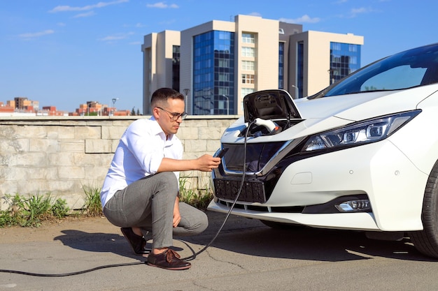 Een man gebruikt een applicatie op zijn telefoon om een elektrische auto op te laden in het concept van groene energie en eco-energie gericht op het verminderen van de CO2-uitstoot