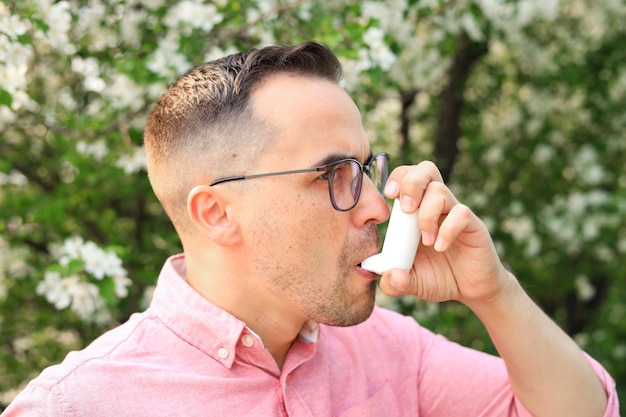 Een man gebruikt een inhalator voor astma in het park vanwege een allergie, een concept dat de effecten van vervuiling, ziekte en ziekte laat zien