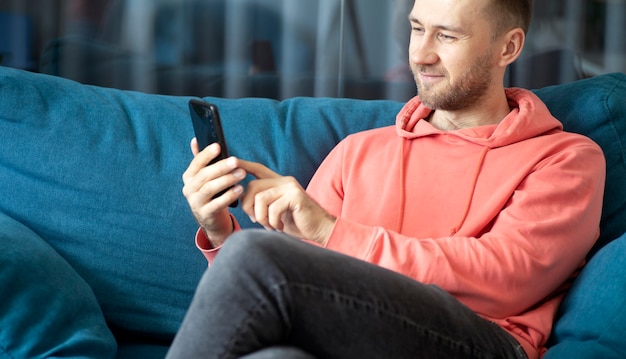 Een man gebruikt een smartphone op zijn thuisbank terwijl hij thuis ontspant, toepassingen noemen internetconcept foto's van hoge kwaliteit