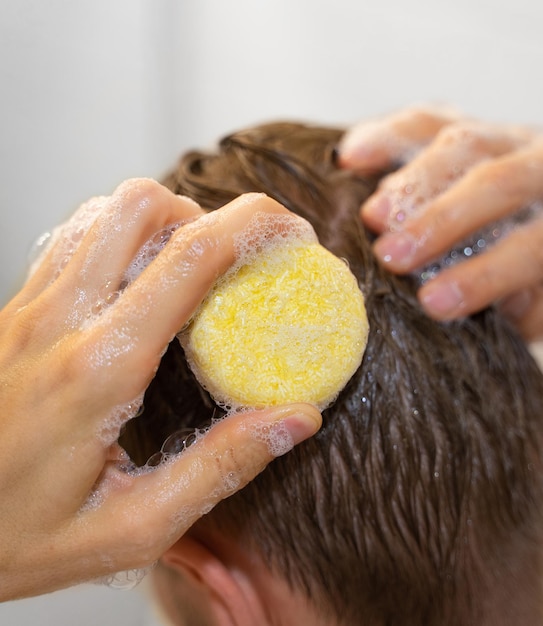 Een man gebruikt een stevige vaste shampoo in de badkamer Een shampoo aanbrengen op de hoofdhuid Plasticvrij, zero waste leven, weinig water bevattende ingrediënten Duurzame haarverzorging Verantwoordelijkheid voor de natuur