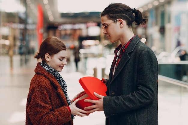 Een man geeft zijn vriendin een hartvormige doos op Valentijnsdag Jong stel in winkelcentrum