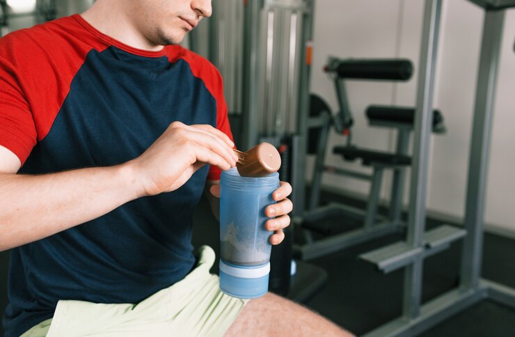Een man giet proteïne in een shaker na een training terwijl hij op een bankje in de sportschool zit. sport-supplementen