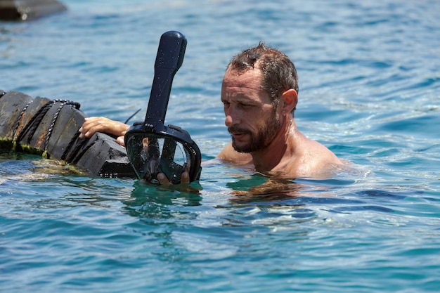 Foto een man haalt zijn duikmasker af en kijkt ernaar water druppelt naar beneden zwarte bril en een snorkel zijn ogen weerspiegelen een mix van verwondering en dankbaarheid voor de verborgen schoonheid die hij net heeft ervaren in de zee