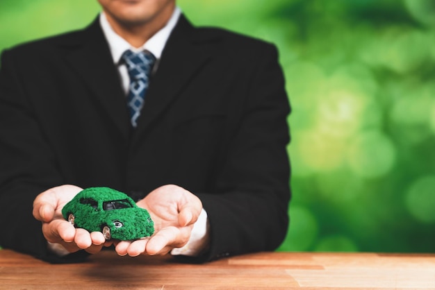 Een man houdt een groene auto vast, gemaakt door een man in pak.