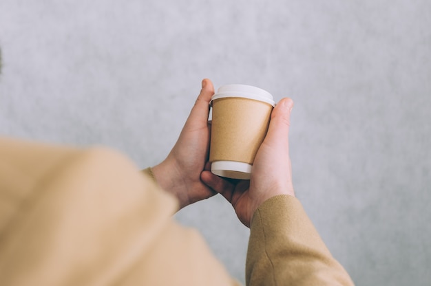 Een man houdt een mock-up van een kartonnen beker voor koffie en thee aan een lamp vast.