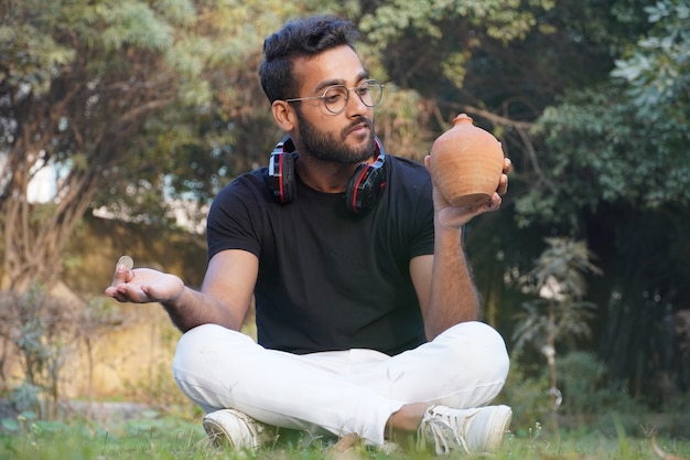 Een man houdt een oortelefoon op zijn schouder en deponeert het geld op zijn spaarvarken