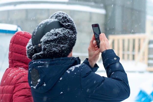 Een man houdt een telefoon, een smartphone in zijn handen, in de kou, in de winter, in een warme jas en muts.