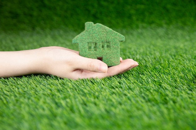 Een man houdt in zijn hand een klein eco-huis op een achtergrond van gras.