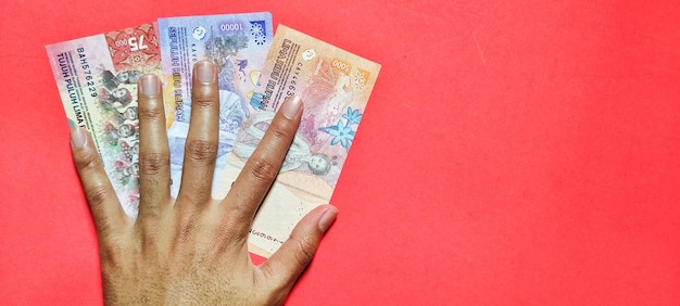 Een man houdt nieuwe bankbiljetten rupiah valuta concept geïsoleerd op een rode achtergrond