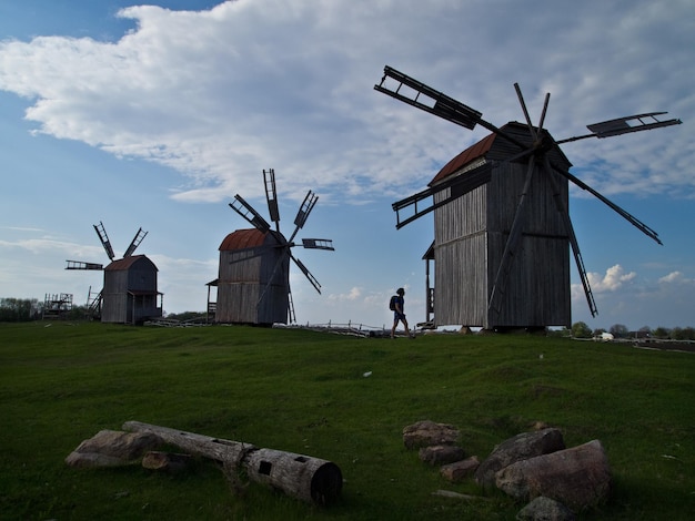 Een man in de buurt van drie Oekraïense traditionele houten windmolens tegen de blauwe lucht traditionele Oekraïense