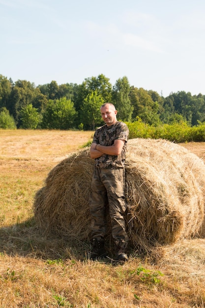 Een man in de buurt van een hooiberg in militaire kleding vroege zomerochtend in het veld