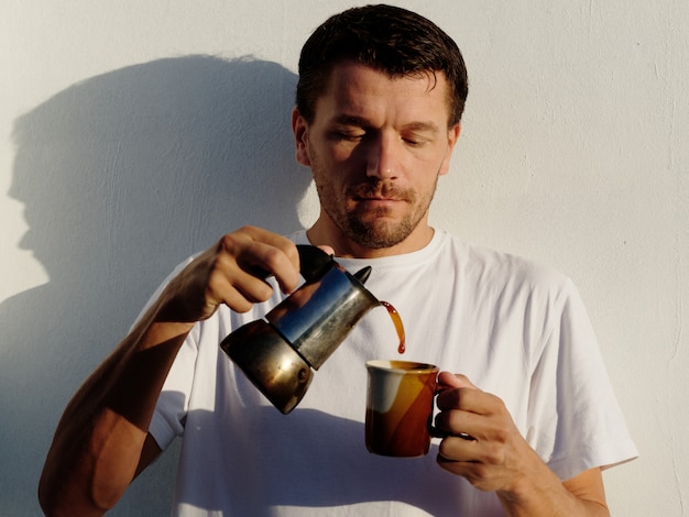 Een man in de ochtend bij zonsopgang giet koffie in een bruin glas.