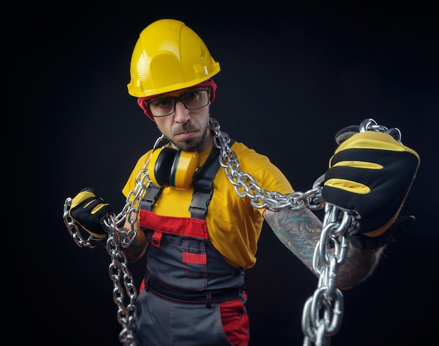 Een man in de overall van een bouwreparateur houdt een metalen ketting in zijn handen