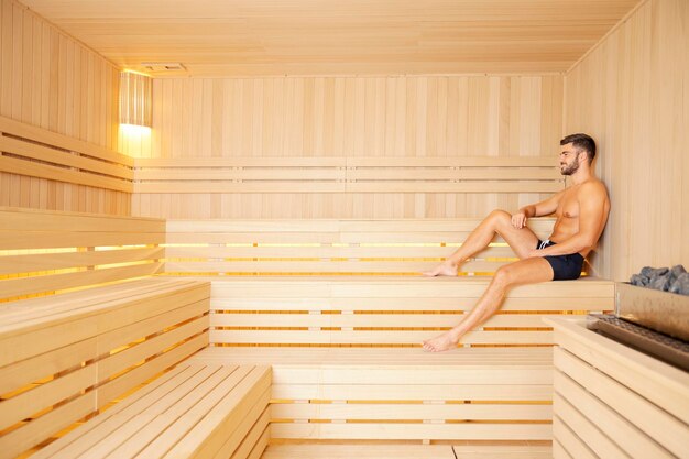 Een man in de spa die gezond blijft Een knappe gespierde man in badkleding die in een sauna zit en ontspant