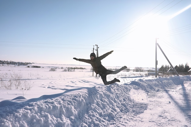 Een man in de winter op straat. De man loopt op de winterweg. Een jonge man in een donsjack springt in de sneeuw.
