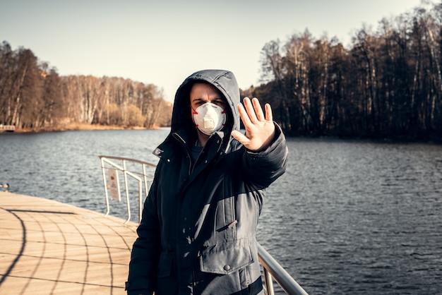 Een man in een beschermend masker in een leeg park. Aan de kust bij het water. Coronavirus pandemie.