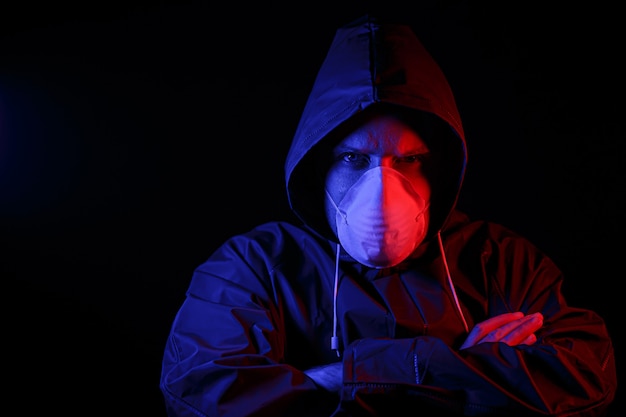 Een man in een beschermend rubberen pak en een wit medisch masker. Virus bescherming. Verlicht in rood en blauw.