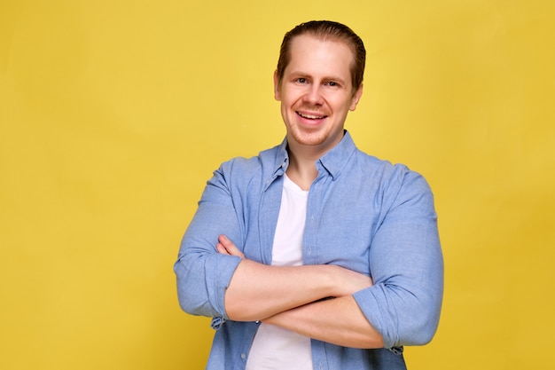 Een man in een blauw shirt op een gele achtergrond geklemd handen glimlacht vrolijk naar de camera.