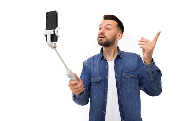 Een man in een blauw spijkerhemd zendt een video uit terwijl hij een smartphone op een selfiestick houdt