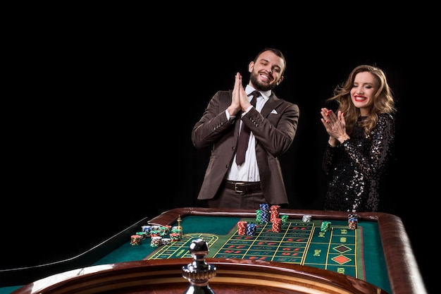 Een man in een bruin pak met een mooie vrouw in een zwarte jurk speelt aan een roulettetafel in een casino. Emotie van gokspelers