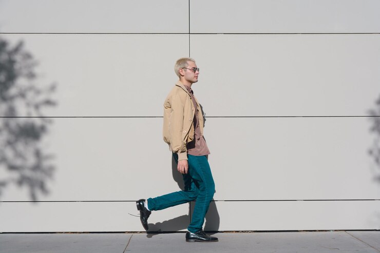 Een man in een bruine jas en blauwe spijkerbroek loopt over een stoep
