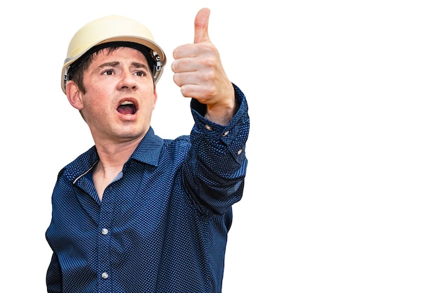 Een man in een constructiehelm op een witte geïsoleerde muur met een opgeheven hand toont zijn duim. De voorman. Bouwer. Ingenieur.
