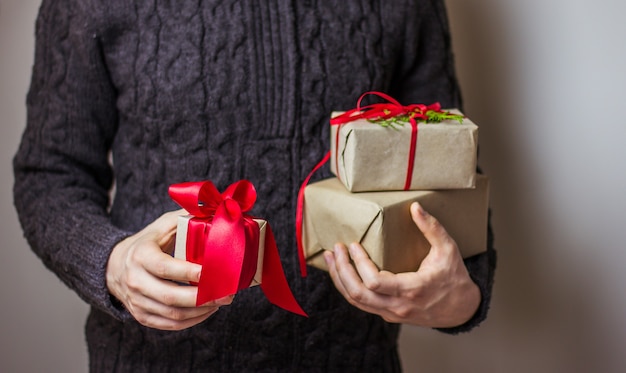 Een man in een donkergrijze trui houdt een geschenkdoos met een rood lint vast