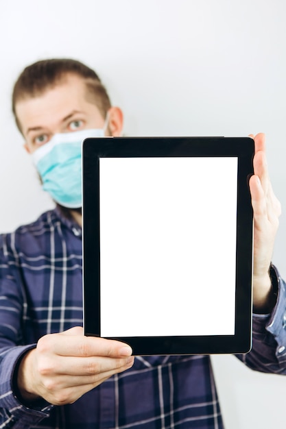 Een man in een geruit overhemd heeft een tablet in zijn handen, op een witte achtergrond. Blijf thuis. Plaats voor tekst. Het zakelijke probleem houdt verband met het coronavirus. COVID-19