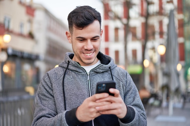 Een man in een grijze hoodie lacht naar zijn telefoon terwijl hij naar zijn telefoon kijkt.