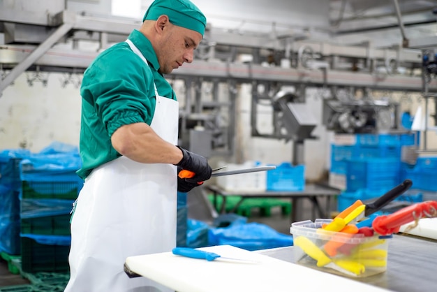 Een man in een groen pak staat in een fabriek met een mes in zijn hand.