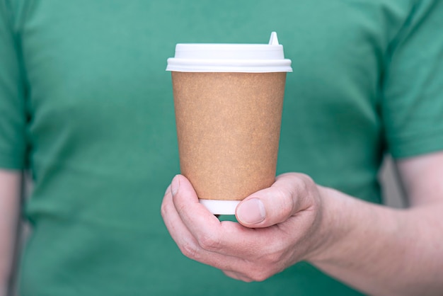 Een man in een groen t-shirt met een papieren bruine kop met koffie of thee close-up