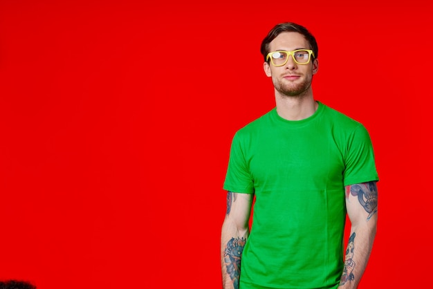 Foto een man in een groen t-shirt met tatoeages in zijn handen met een bril op een rode achtergrond foto van hoge kwaliteit