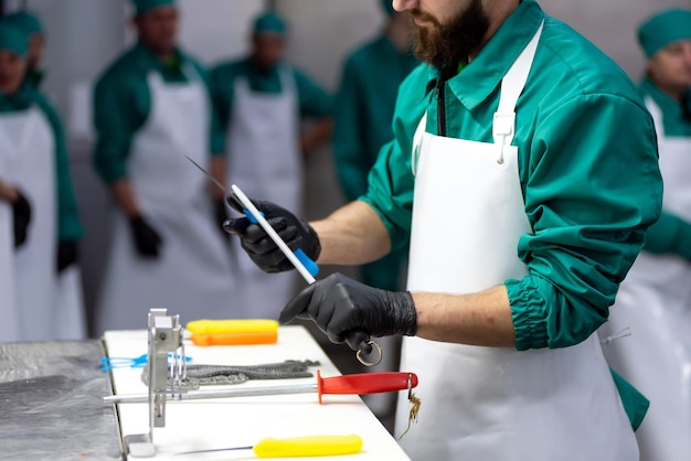 Een man in een groen uniform houdt een mes in zijn hand terwijl op de achtergrond een groep mensen toekijkt.