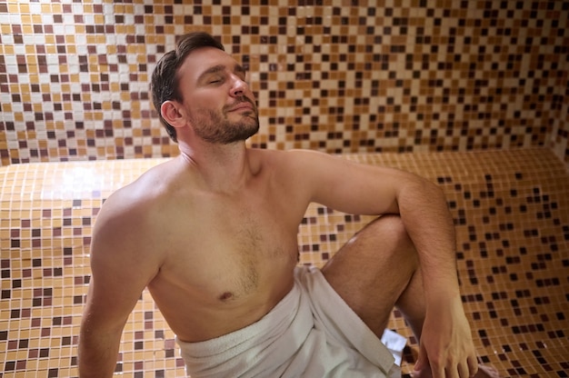 Een man in een handdoek die in de sauna zit en een detox-sessie heeft