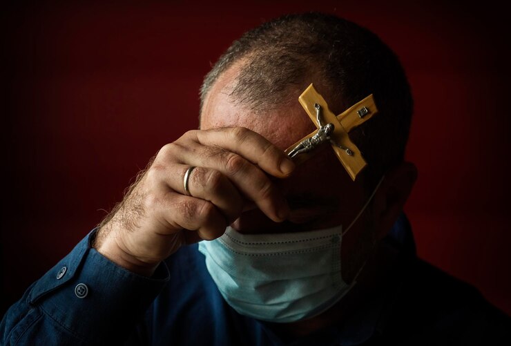 Foto een man in een medisch masker met een katholiek kruis bedekte zijn gezicht met zijn hand