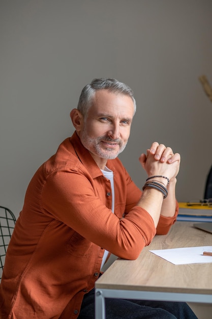 Een man in een oranje shirt die aan tafel zit en er tevreden uitziet