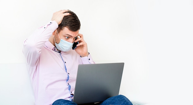 Een man in een overhemd en spijkerbroek werkt op de laptop en spreekt aan de telefoon