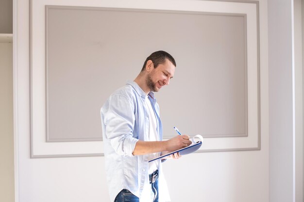 Een man in een overhemd staat in een kamer met een map en maakt aantekeningen